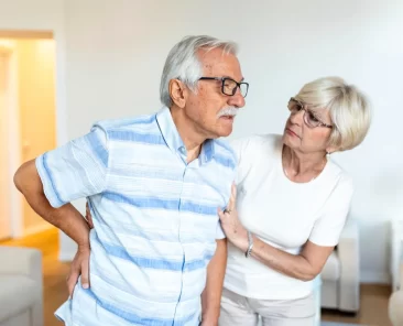 Um homem idoso sente dor na coluna e é amparado pela sua esposa.
