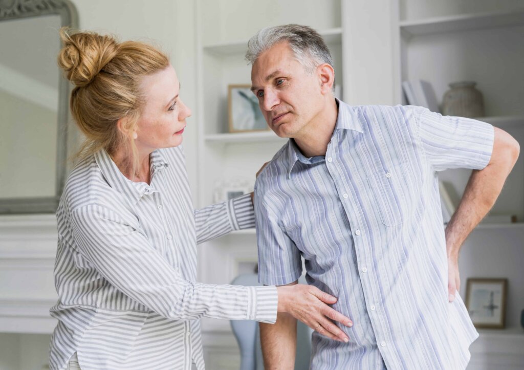 Um homem sofre com escoliose e é ajudado pela esposa.